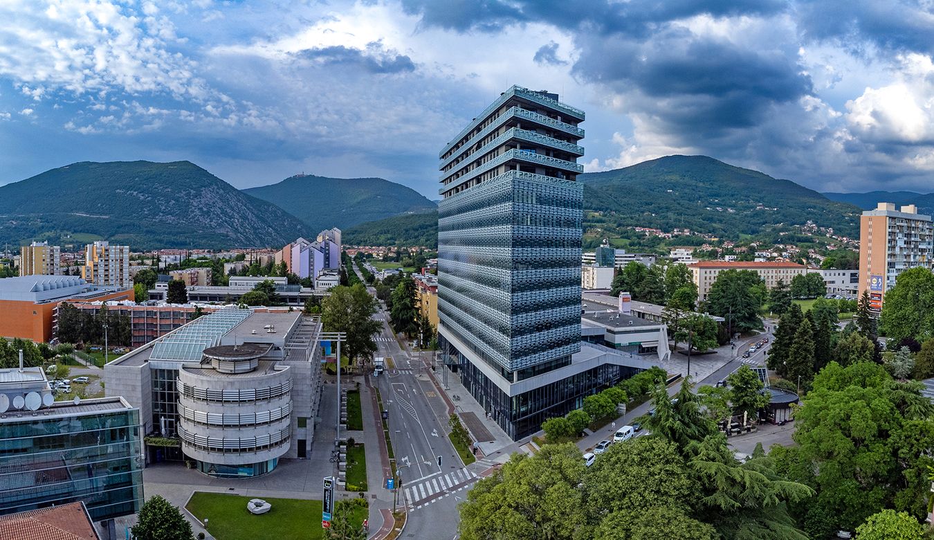 Panoramski pogled na stavbo Eda, Nebotičnik in druge zgradbe v Novi Gorici,  Sabotin in Sveto Goro v ozadju.