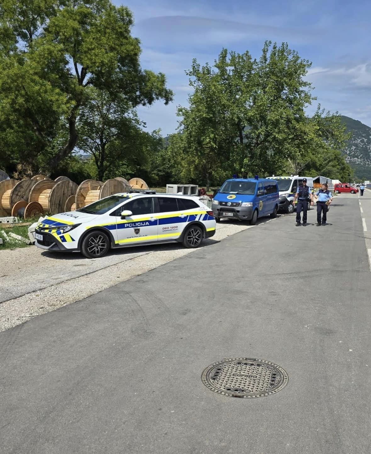 Policijska vozila, parkirana ob robu ceste. Policisti nadzorujejo območje.