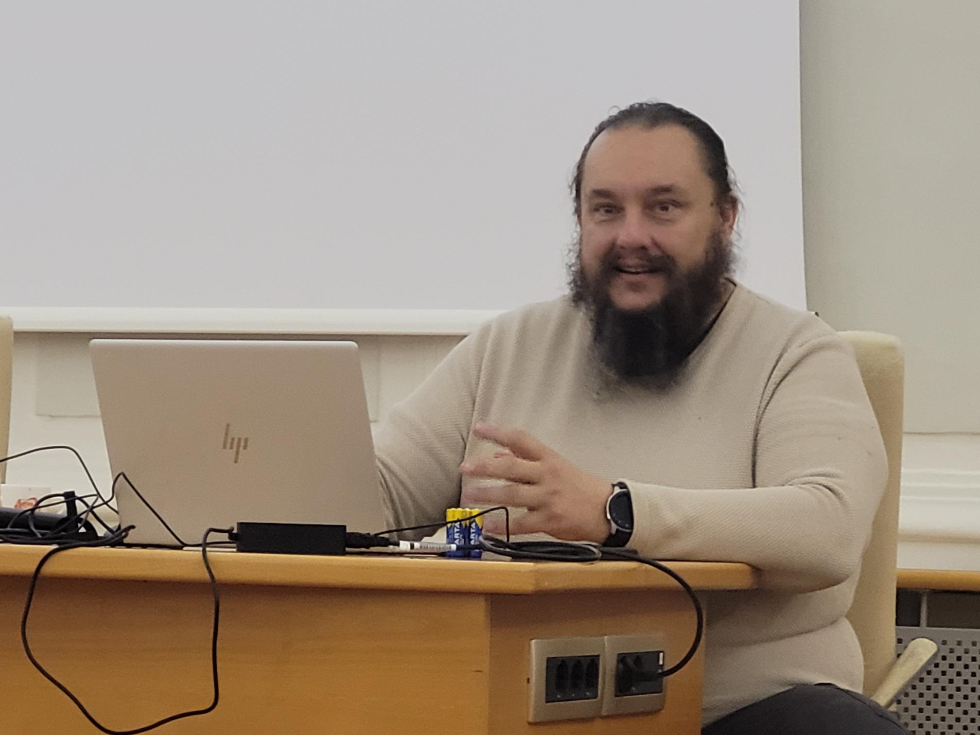 Predavatelj o digitalni dostopnosti Tilen Škraba sedi za mizo in predava v veliki dvorani mestne občine
