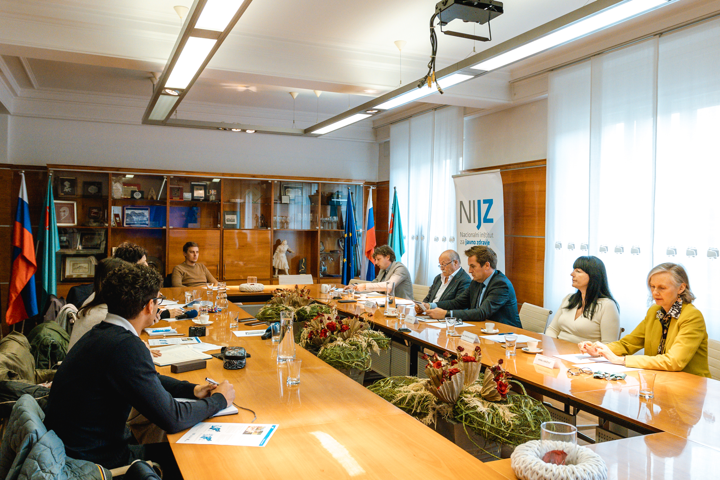 Udeleženci novinarske konference sedijo za veliko mizo v Stekleni dvorani na Mestni občini Nova Gorica